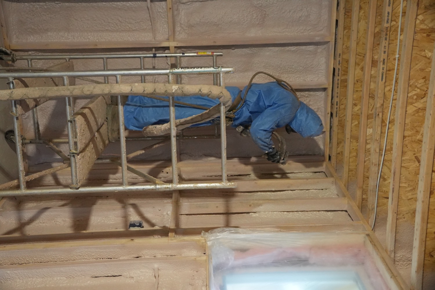 Applicator in a protective suit spraying foam into a framed wall