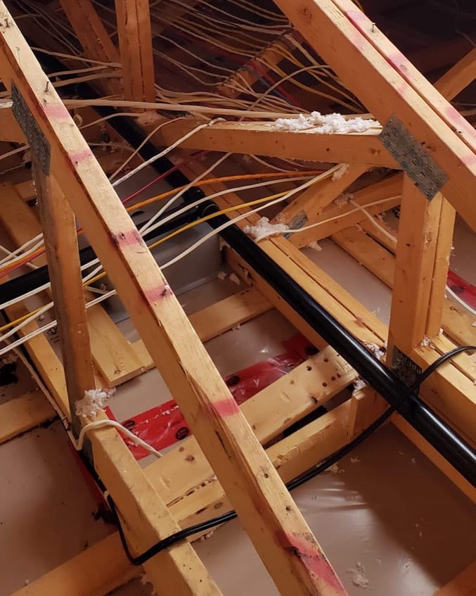 Attic trusses over a taped ceiling vapour barrier with wiring run and penetrations foamed, the stage when attic insulation baffles and air sealing have to be finished before blowing