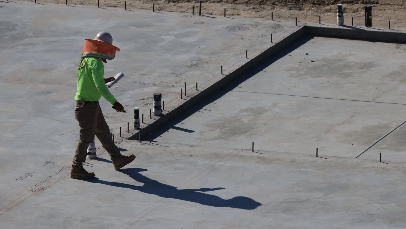 Finished slab on grade with plumbing stubs and anchor bolts along a formed edge, a worker checking the layout