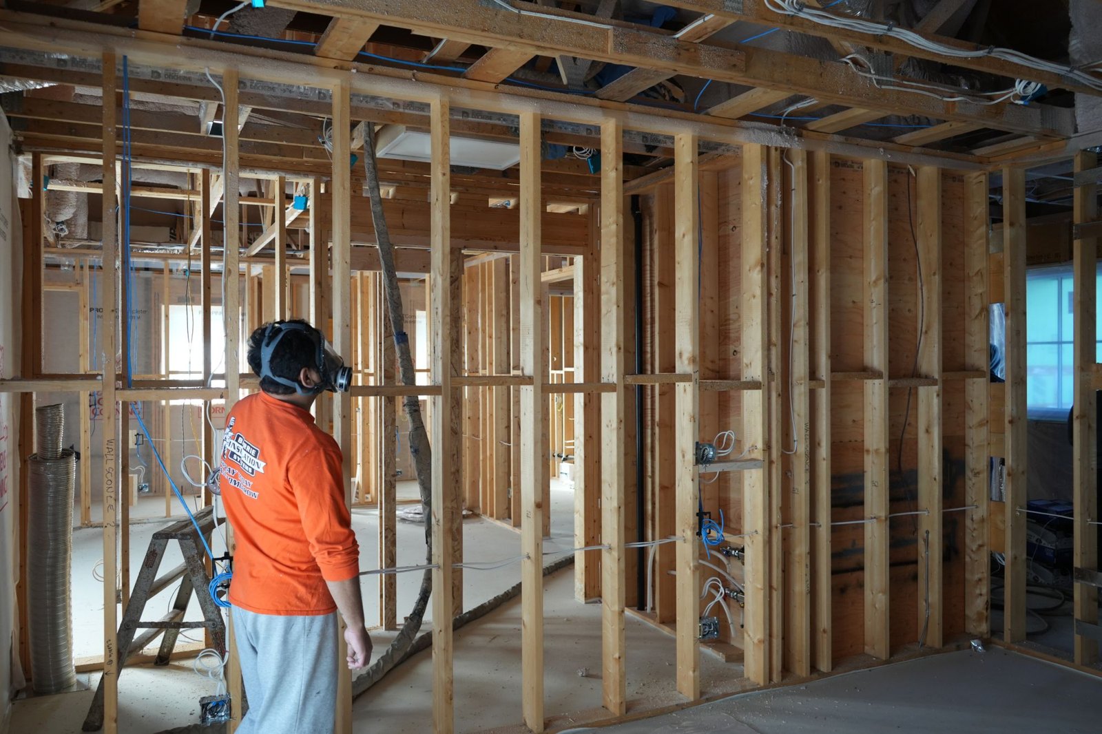 Barrie Insulation Systems crew member in a respirator in a framed renovation with the wiring and ductwork roughed in, the stage where how long does spray foam take to cure meets the rest of the schedule