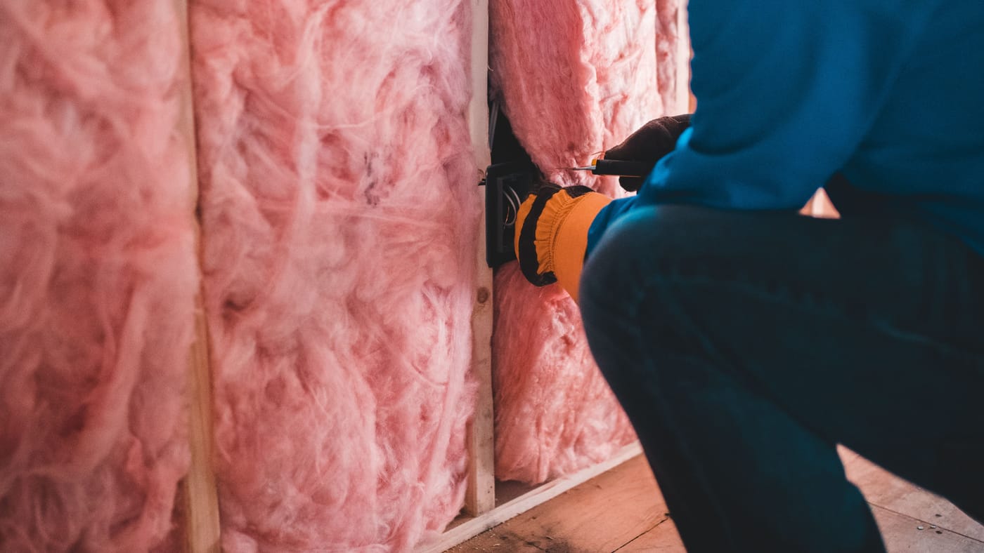 Fibreglass batts being cut around an electrical box in a stud wall, the cheaper alternative to mineral wool batt insulation on most exterior walls