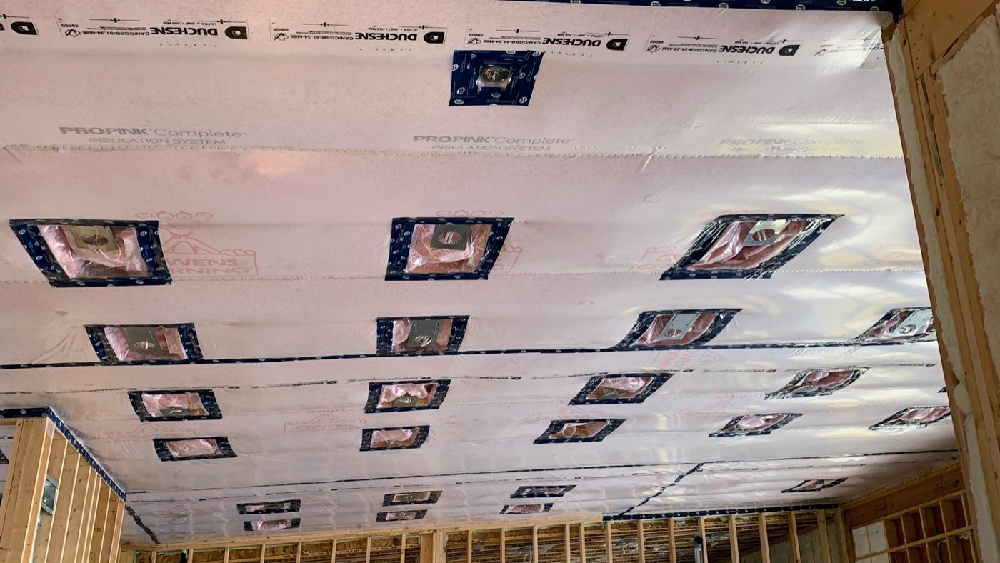 Top-floor ceiling with poly vapour barrier over batt insulation, the poly cut and taped around each pot light opening in rows across the joists