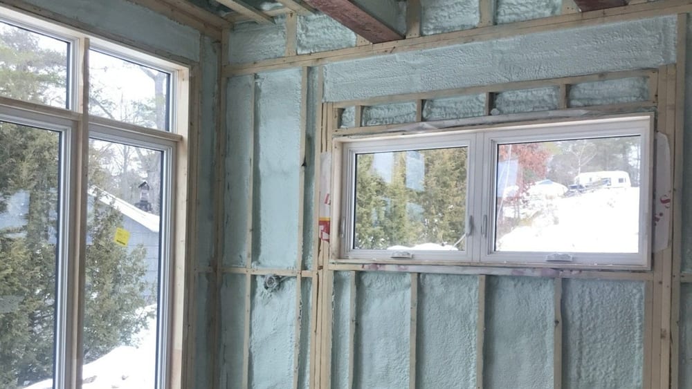 Two windows in a framed exterior wall, with closed cell spray foam filling the stud bays and the header around the rough openings