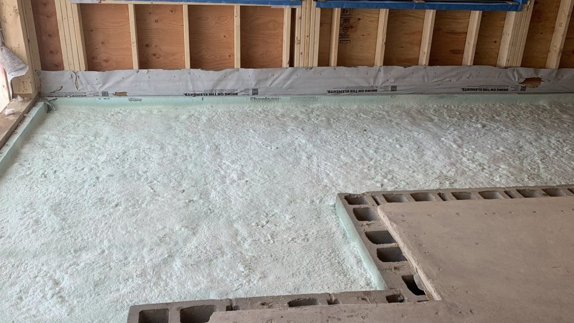 Vapour barrier basement floor ahead of the pour: an even layer of spray foam over the sub-base, run tight to the foam board and sheathing membrane at the base of the wall