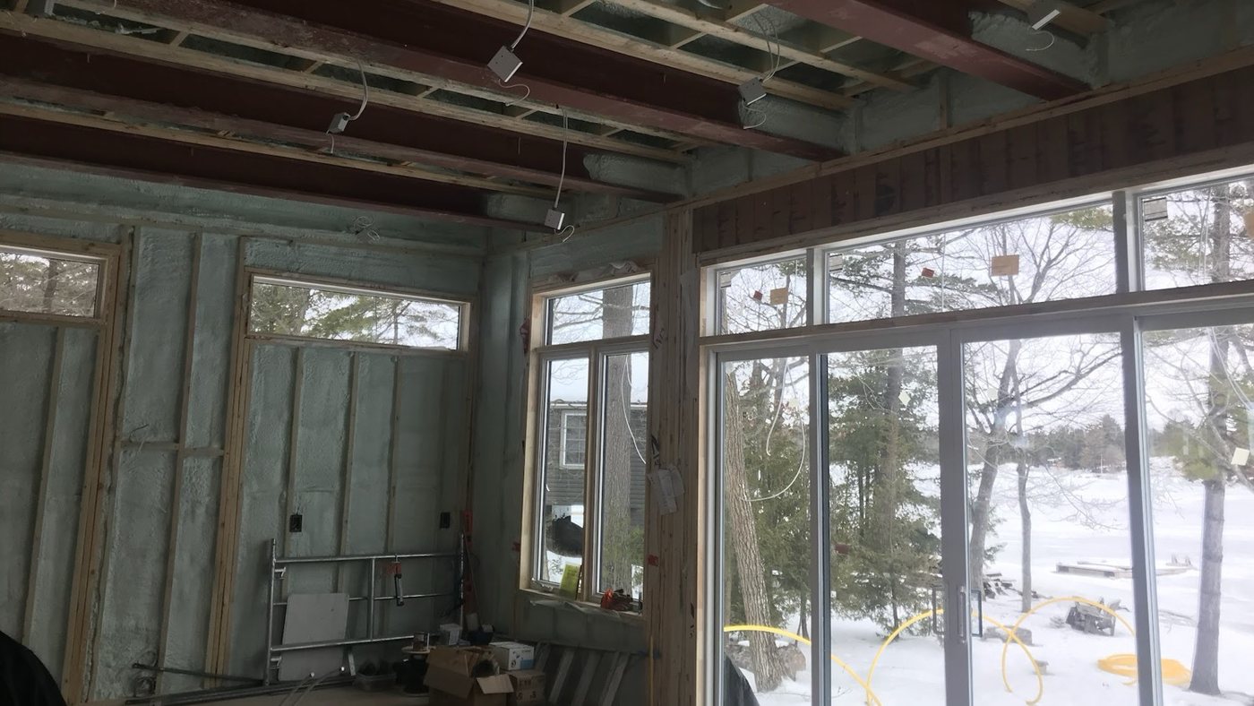 Great room in a new build with spray foam filling the exterior stud walls, two outlet boxes set in the foamed bays and electrical rough-in hanging from the ceiling framing