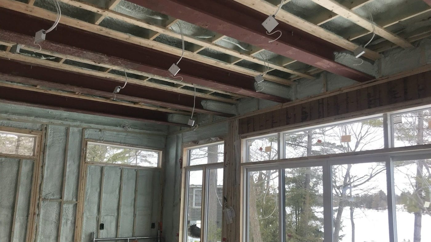 Cottage great room under construction with spray foam filling every exterior wall cavity and the ceiling bays between the beams, no poly over it, the foam itself acting as the vapour retarder